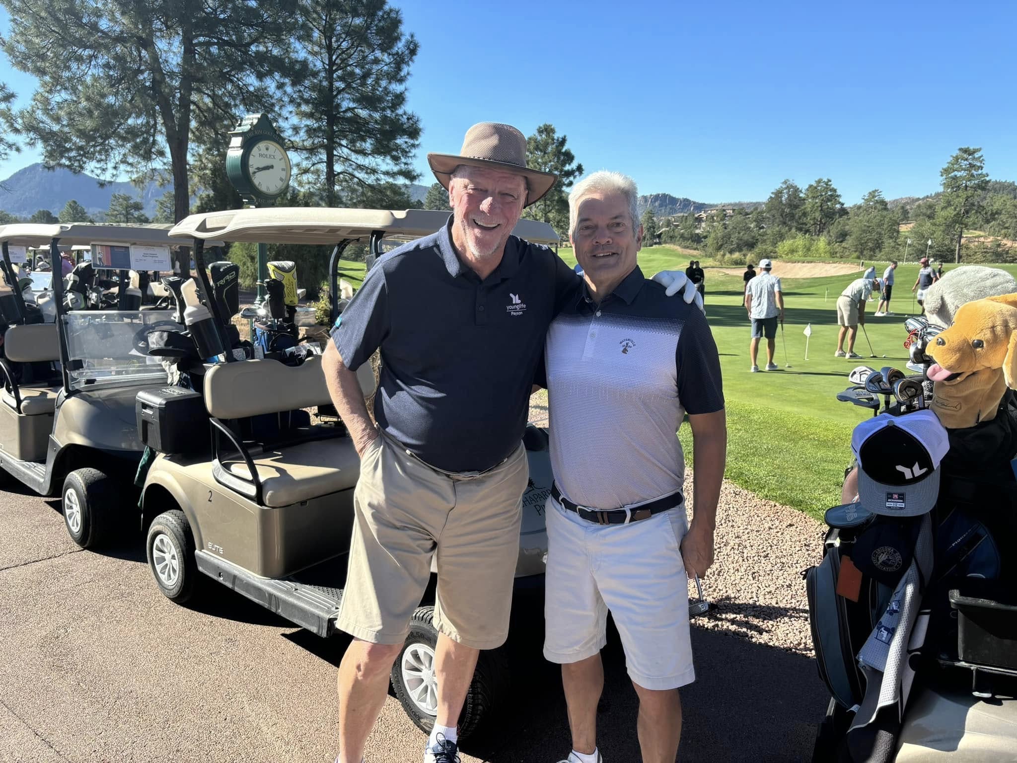 Two golfers smiling together beside a row of tournament golf carts